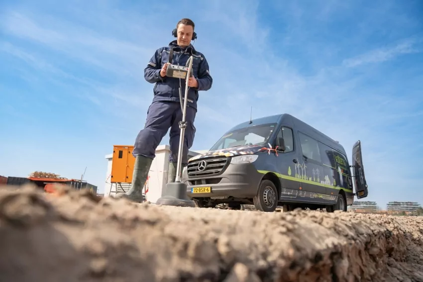 Monteur met een kabelzoekapparaat bij een bestelbus op een bouwterrein