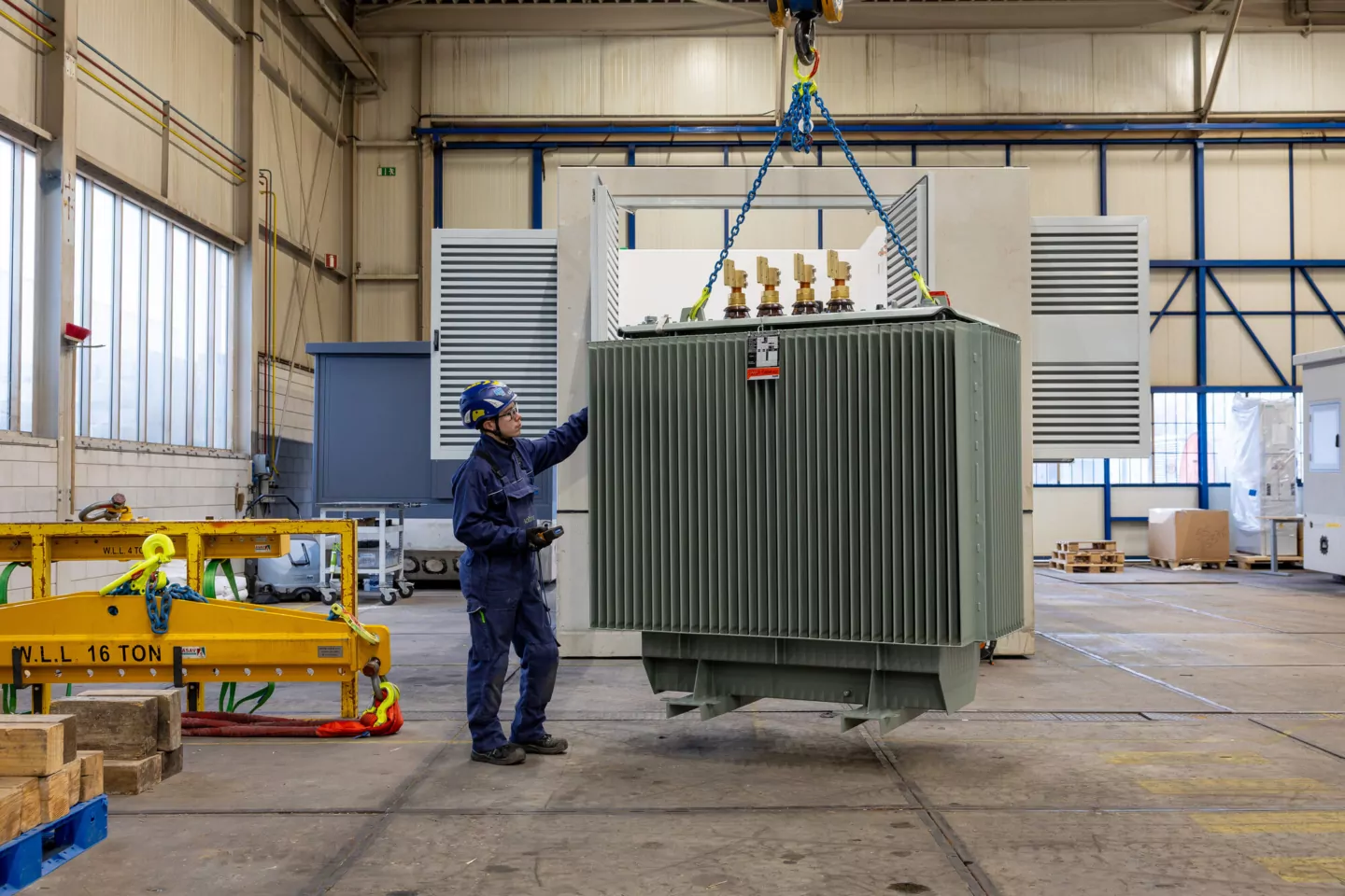 Monteur begeleidt een transformator die met een hijskraan wordt verplaatst