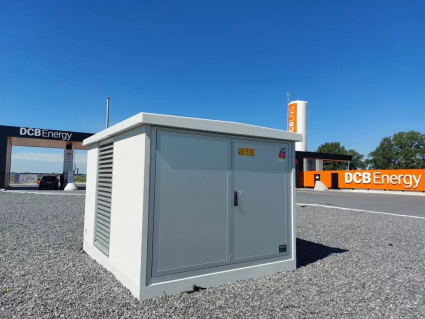 Grijs transformatorstation op een grindterrein bij een tankstation